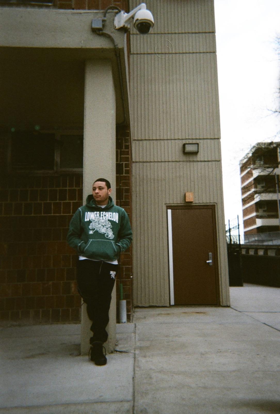 Model in a Day n Night sweatsuit leaning against a brick building
